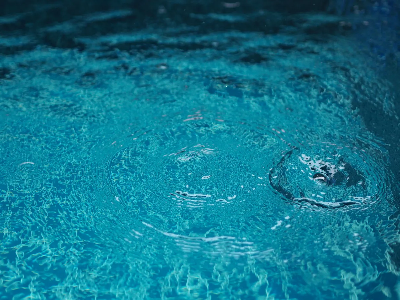 Rain drops falling blue water in pool background r 2026 03 20 00 46 03 utc